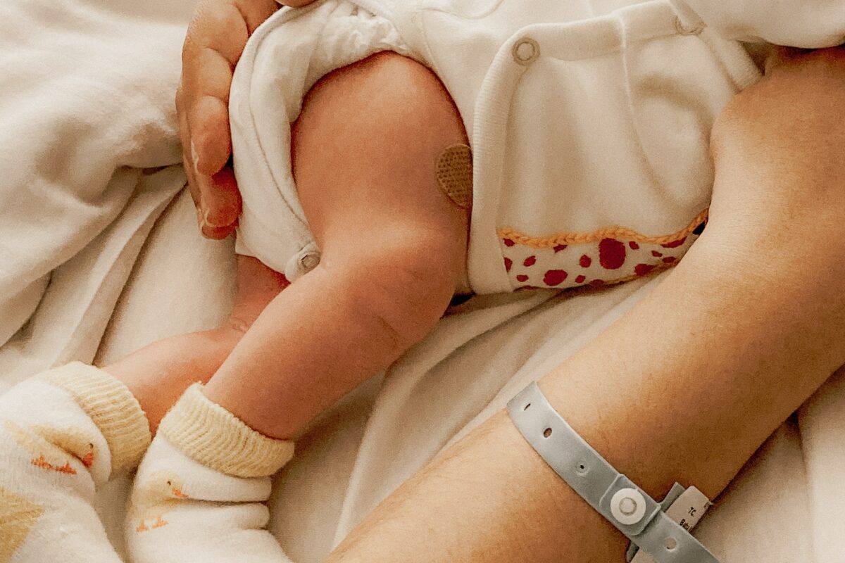 Personne qui tient dans ses bras un bébé naissant vêtu d'un pyjama. On voit un bracelet d'hôpital à son poignet.