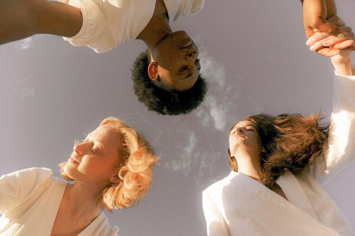 Vue vers le haut de la tête de trois personnes vêtues de blanc. On voit un ciel bleu en arrière-plan.