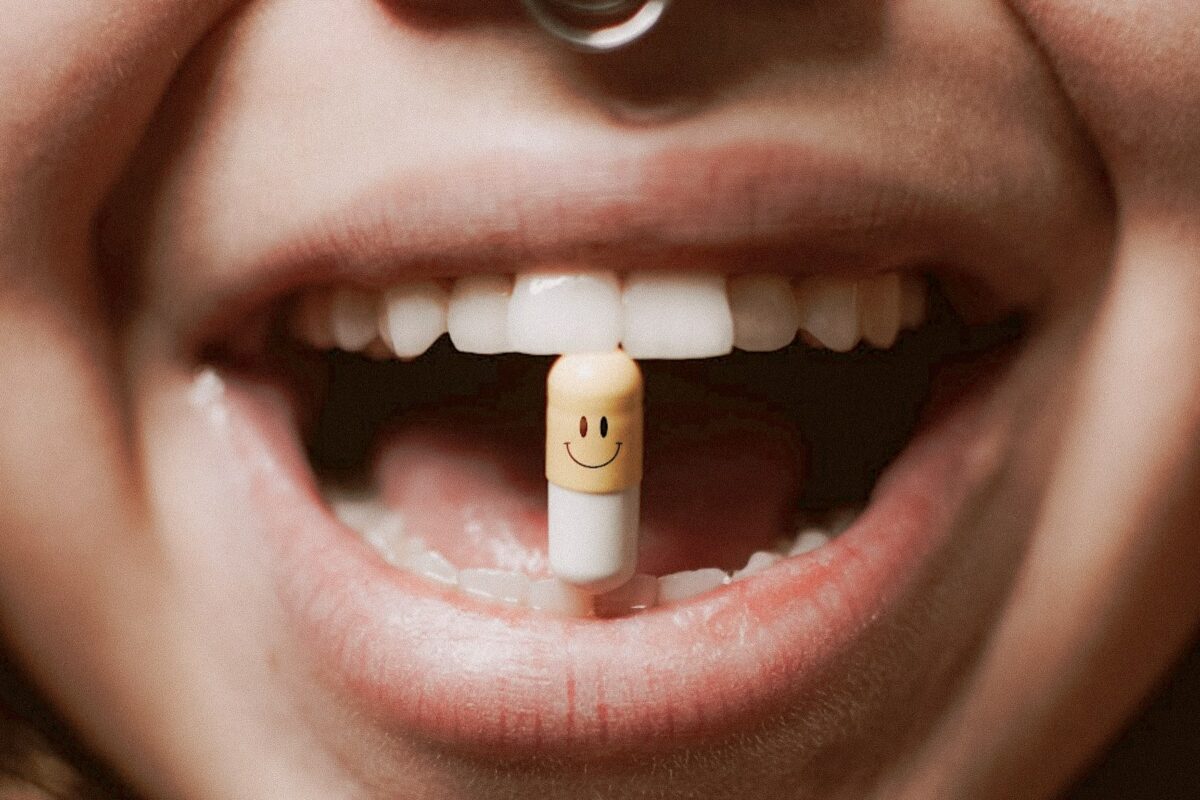 Gros plan sur la bouche d'une personne qui tient une pilule avec un bonhomme sourire entre ses dents.