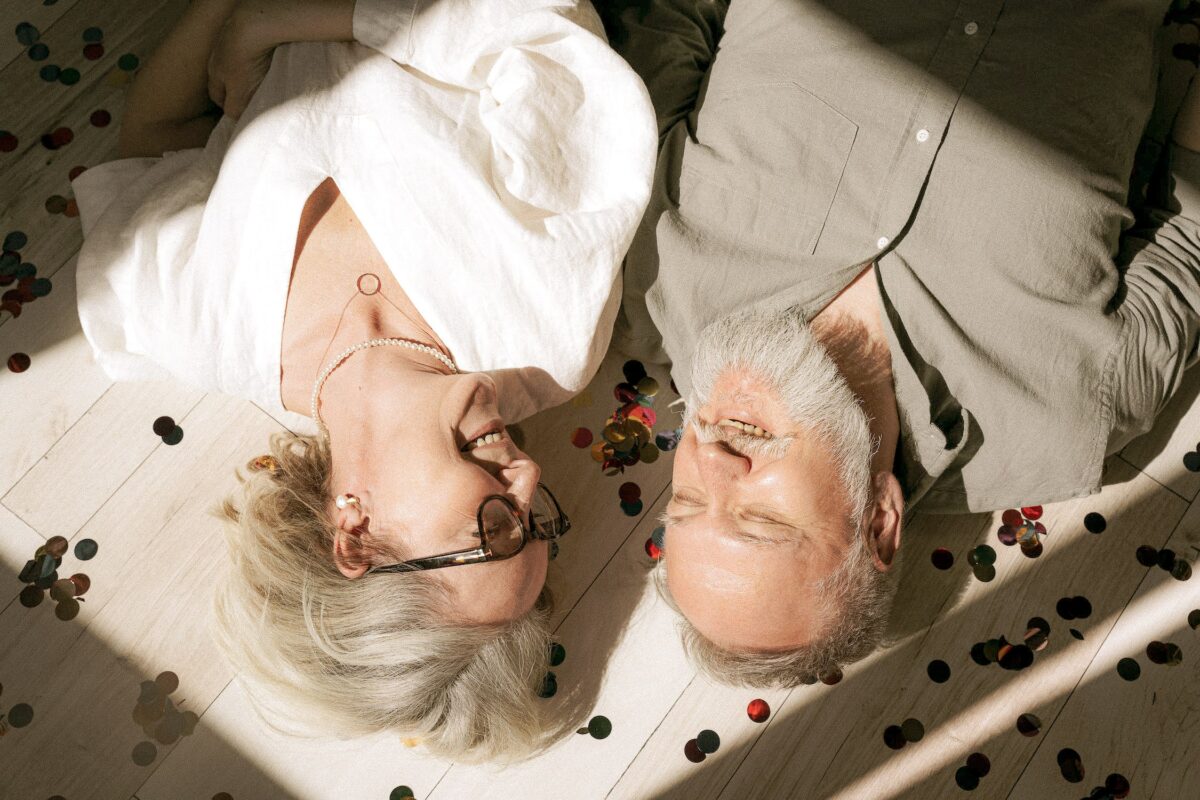 Deux adultes âgé·e·s sont couché·e·s sur le plancher et se regardent en riant.